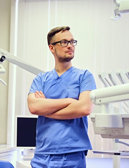 Handsome male dentist in a room with medical equipment on background.