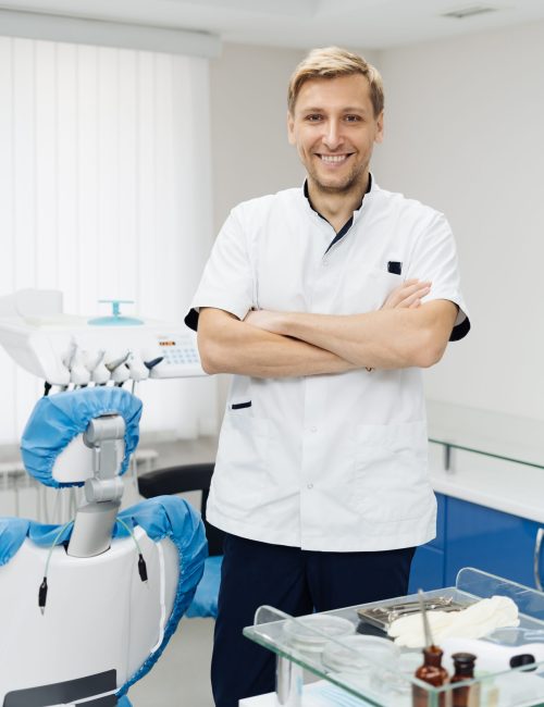 Portrait of a positive young male dentist in uniform with crossed hands at the dental office